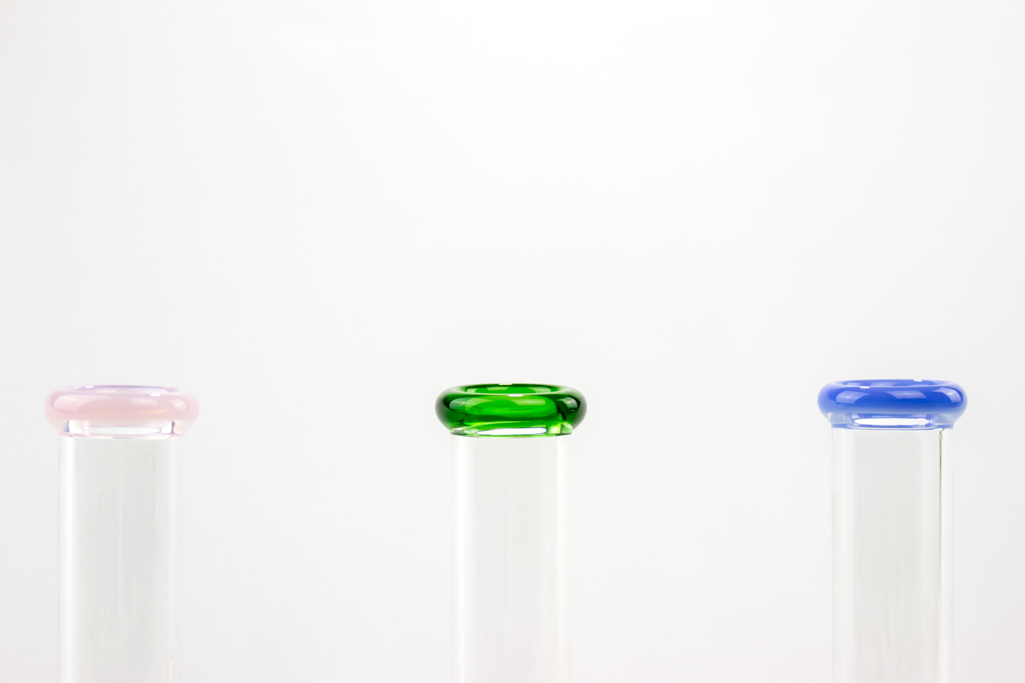 Three Flow3r beakers with pink, green, and blue glass rims on a clean white background
